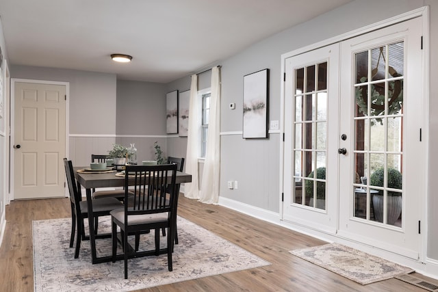 dining space with french doors, wainscoting, and light wood-style flooring