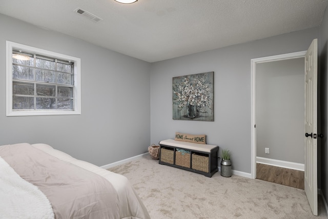 carpeted bedroom featuring a textured ceiling, visible vents, and baseboards