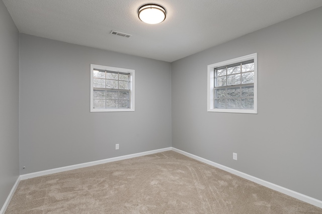 spare room with light carpet, plenty of natural light, visible vents, and baseboards