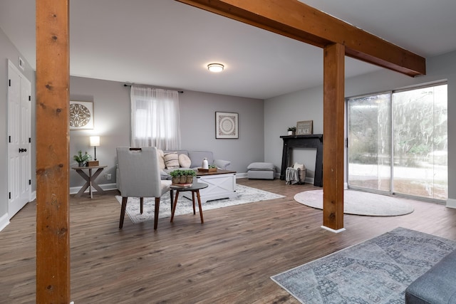 living area featuring dark wood-style flooring, beamed ceiling, and baseboards