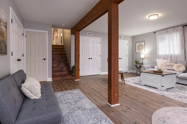 living area featuring wood finished floors, visible vents, baseboards, stairway, and beam ceiling