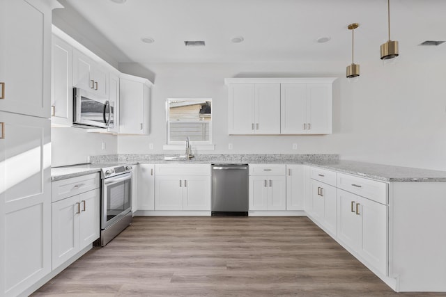 kitchen featuring white cabinets, light wood-type flooring, decorative light fixtures, light stone counters, and stainless steel appliances