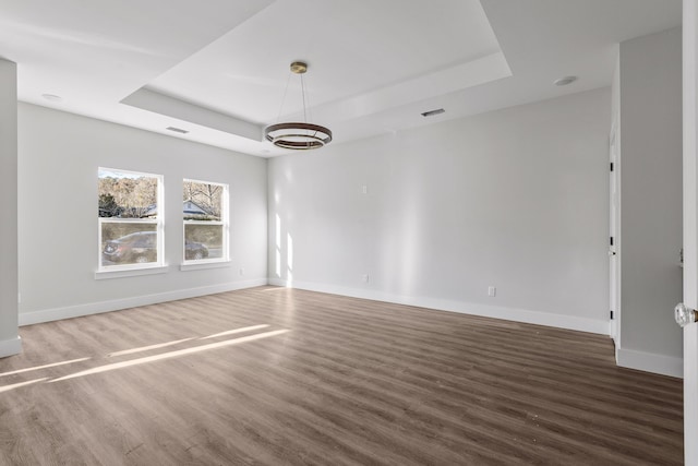 unfurnished room with a chandelier, dark hardwood / wood-style flooring, and a tray ceiling