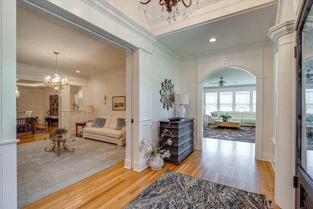 foyer entrance with ceiling fan with notable chandelier, hardwood / wood-style flooring, ornate columns, and crown molding