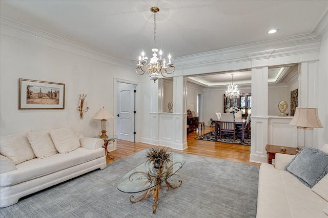 living room with ornate columns, crown molding, light hardwood / wood-style floors, and a notable chandelier