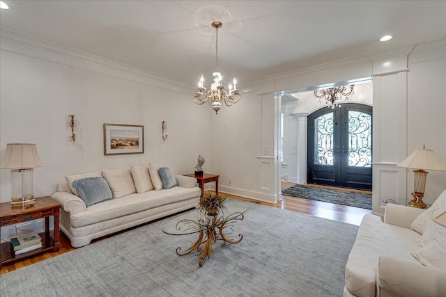 living room with hardwood / wood-style flooring, a notable chandelier, crown molding, and french doors