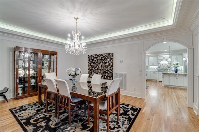 dining area with a chandelier, light hardwood / wood-style floors, crown molding, and a tray ceiling