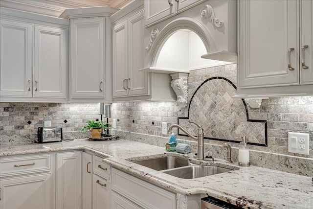 kitchen featuring backsplash, light stone counters, white cabinetry, and sink