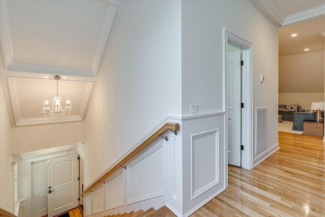 stairway featuring wood-type flooring, ornamental molding, and an inviting chandelier