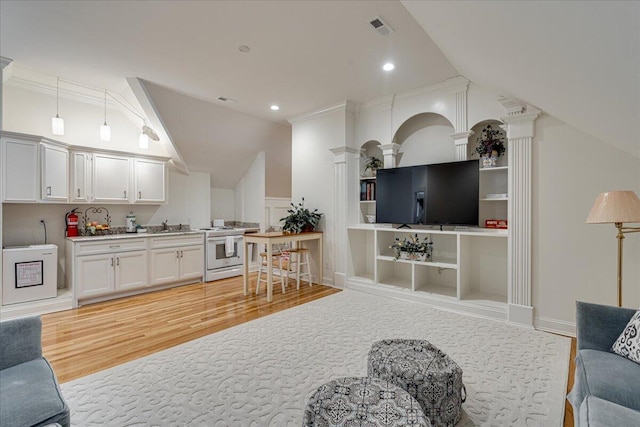 living room with decorative columns, ornamental molding, sink, light hardwood / wood-style floors, and lofted ceiling