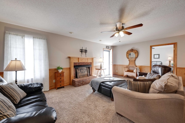 carpeted living room with a textured ceiling, ceiling fan, wooden walls, and a fireplace