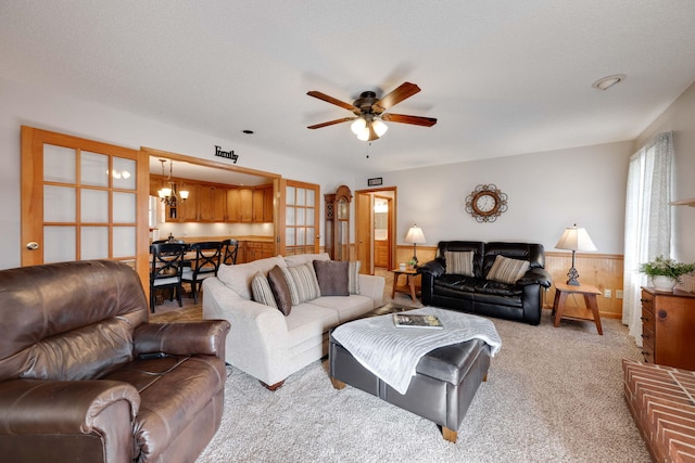 living room with ceiling fan with notable chandelier, wood walls, and light colored carpet