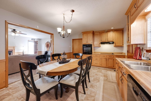 dining area with ceiling fan with notable chandelier, a textured ceiling, wood walls, and sink