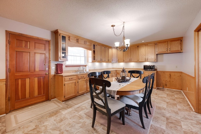 kitchen featuring sink, wooden walls, a textured ceiling, pendant lighting, and a notable chandelier