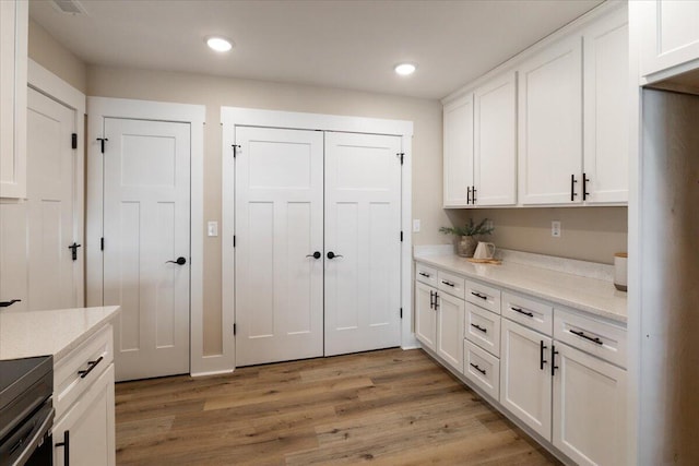 kitchen featuring white cabinetry, light stone counters, and hardwood / wood-style flooring