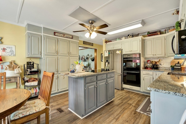 kitchen featuring black appliances, light stone counters, tasteful backsplash, a kitchen island, and dark wood-type flooring