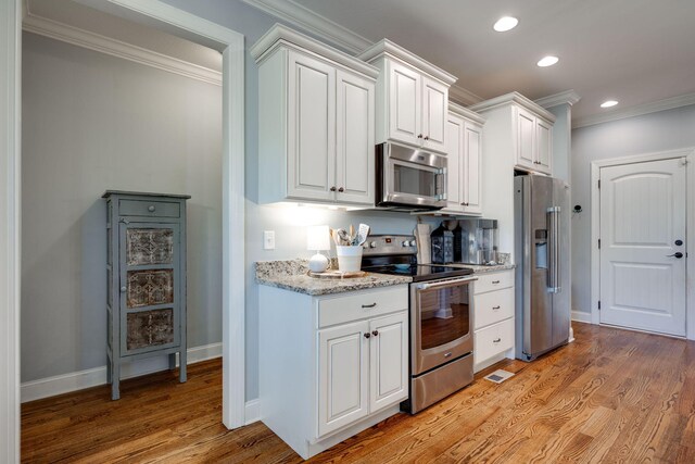 kitchen with light wood-type flooring, light stone counters, ornamental molding, stainless steel appliances, and white cabinets