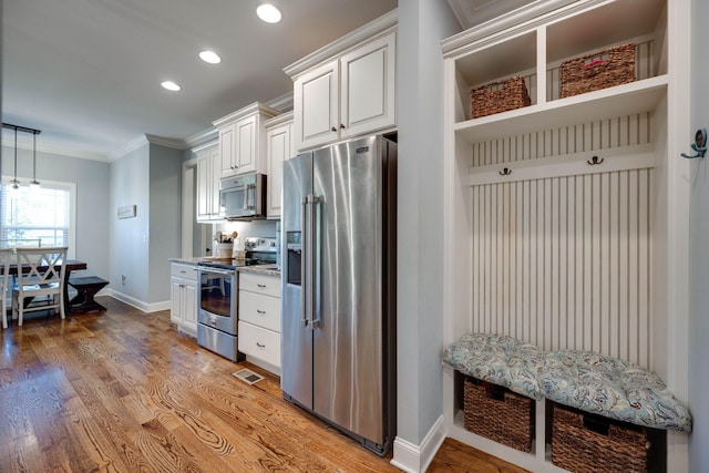 kitchen featuring white cabinets, crown molding, hardwood / wood-style flooring, light stone countertops, and stainless steel appliances