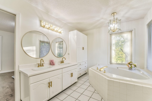 bathroom featuring tiled tub, vanity, a textured ceiling, tile patterned flooring, and a chandelier