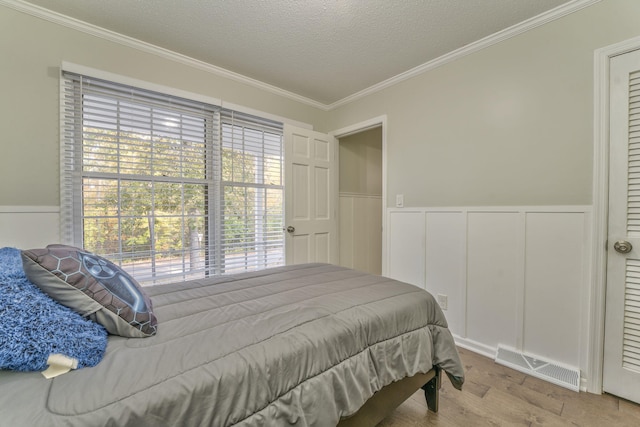 bedroom featuring light wood-type flooring, multiple windows, a textured ceiling, and crown molding