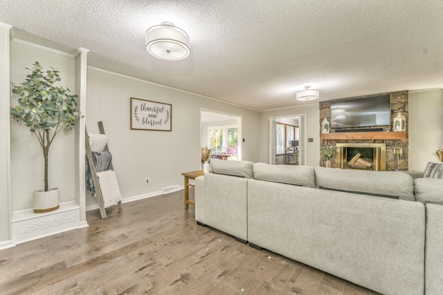 living room with a stone fireplace, wood-type flooring, a textured ceiling, and crown molding