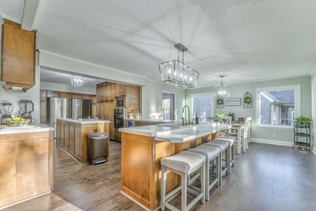 kitchen featuring wood-type flooring, a center island with sink, black oven, a textured ceiling, and hanging light fixtures