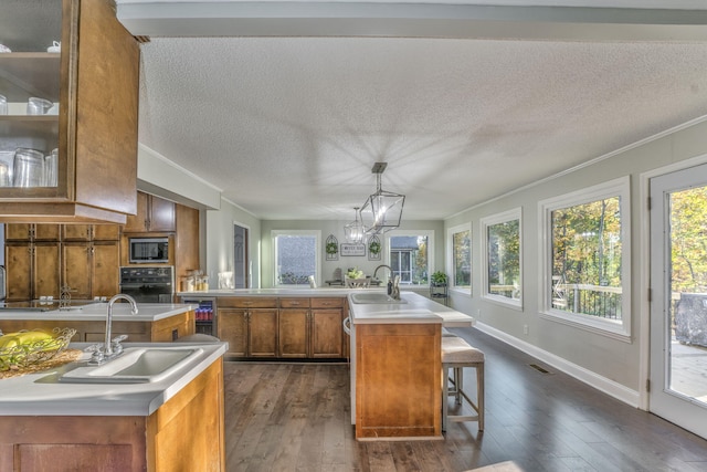 kitchen featuring decorative light fixtures, a center island with sink, sink, and dark hardwood / wood-style floors