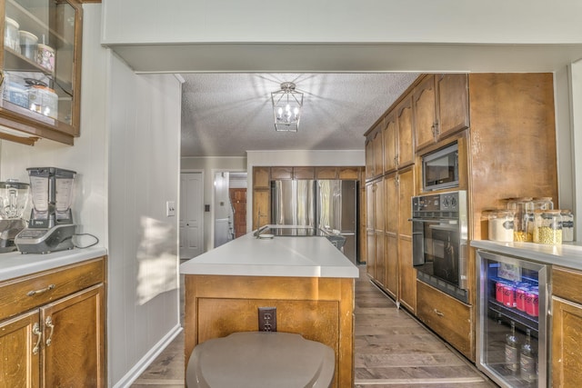 kitchen with stainless steel appliances, beverage cooler, hardwood / wood-style floors, a textured ceiling, and a kitchen island