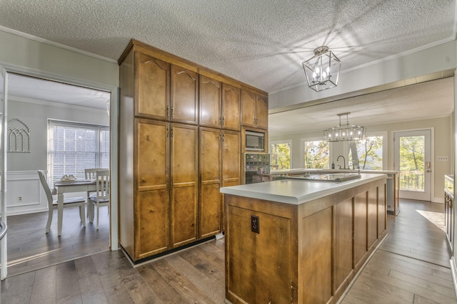 kitchen with a center island with sink, black oven, hanging light fixtures, stainless steel microwave, and dark wood-type flooring