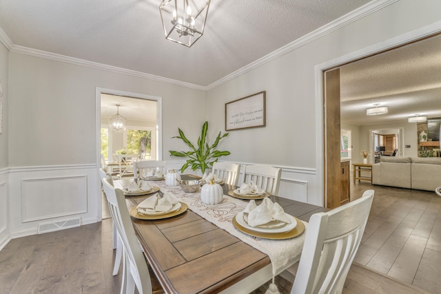 dining space featuring an inviting chandelier, a textured ceiling, crown molding, and wood-type flooring