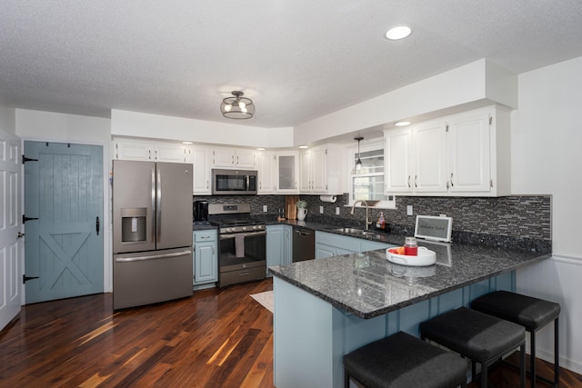 kitchen featuring kitchen peninsula, white cabinets, appliances with stainless steel finishes, and dark wood-type flooring