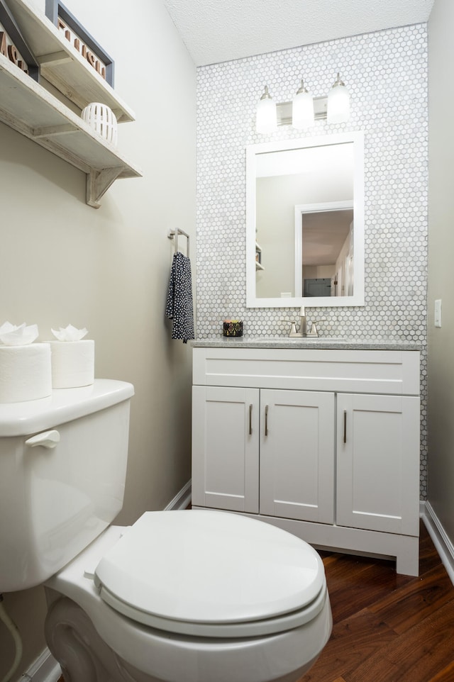 bathroom with wood-type flooring, vanity, toilet, a textured ceiling, and backsplash