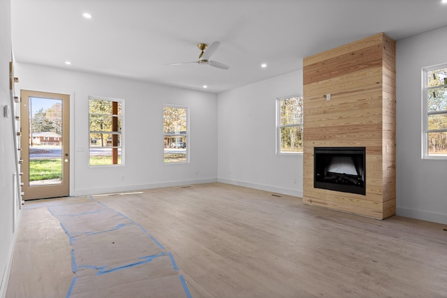 unfurnished living room featuring ceiling fan, a tiled fireplace, and light hardwood / wood-style flooring