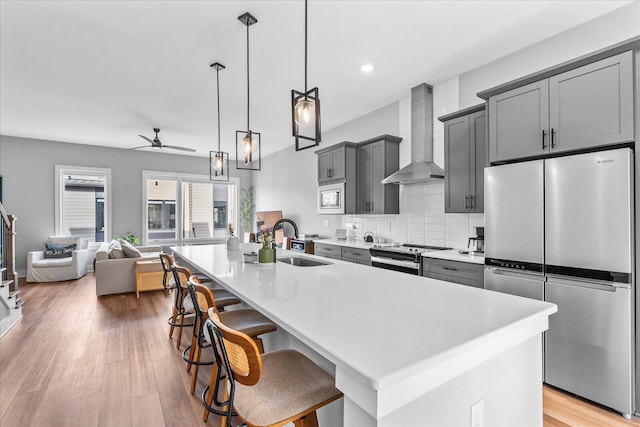 kitchen featuring appliances with stainless steel finishes, wall chimney exhaust hood, a breakfast bar, sink, and an island with sink