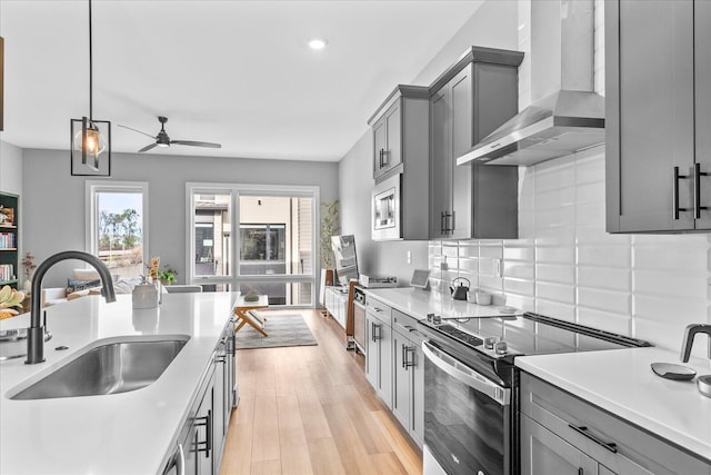 kitchen with wall chimney range hood, sink, gray cabinets, stainless steel electric range oven, and light hardwood / wood-style floors