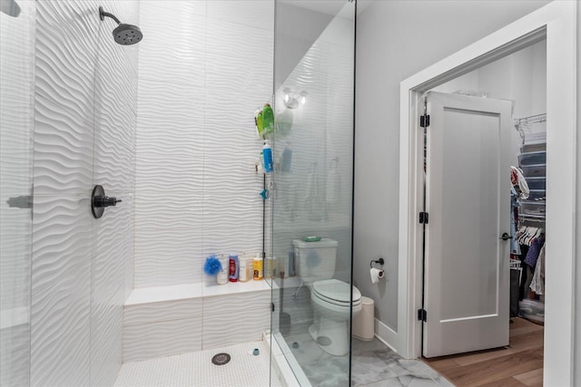 bathroom with hardwood / wood-style flooring, toilet, and a tile shower