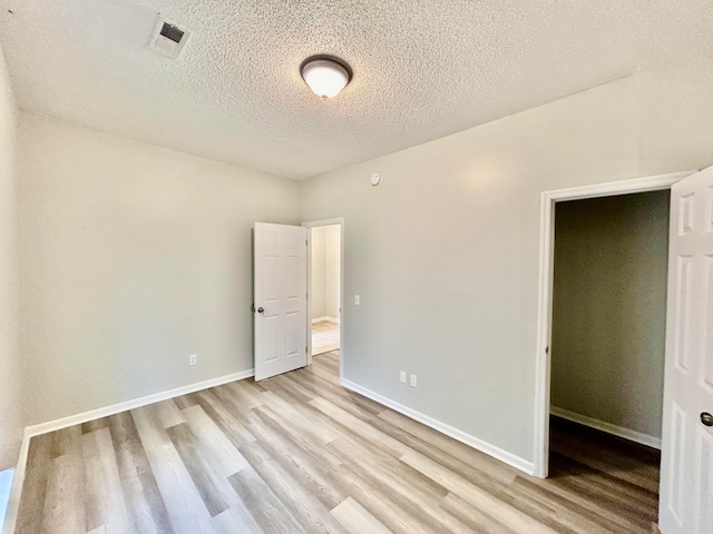 unfurnished bedroom featuring a closet, a textured ceiling, and light hardwood / wood-style floors