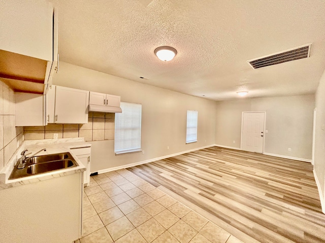 kitchen with tasteful backsplash, a textured ceiling, sink, light hardwood / wood-style floors, and white cabinets