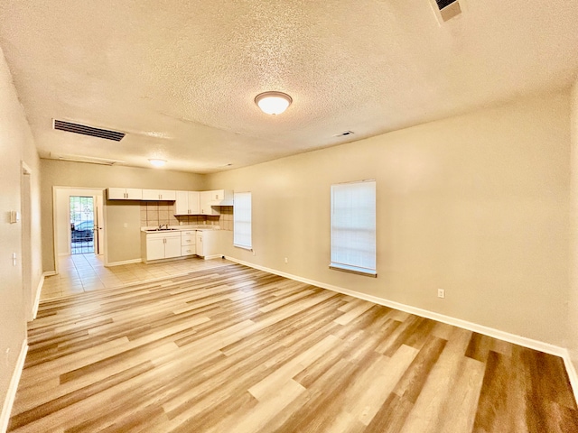 unfurnished living room featuring light hardwood / wood-style floors, a textured ceiling, and sink