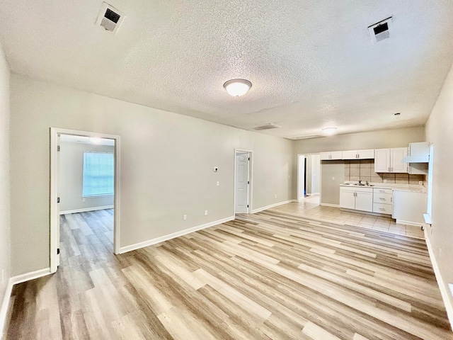 unfurnished living room with a textured ceiling, sink, and light hardwood / wood-style flooring