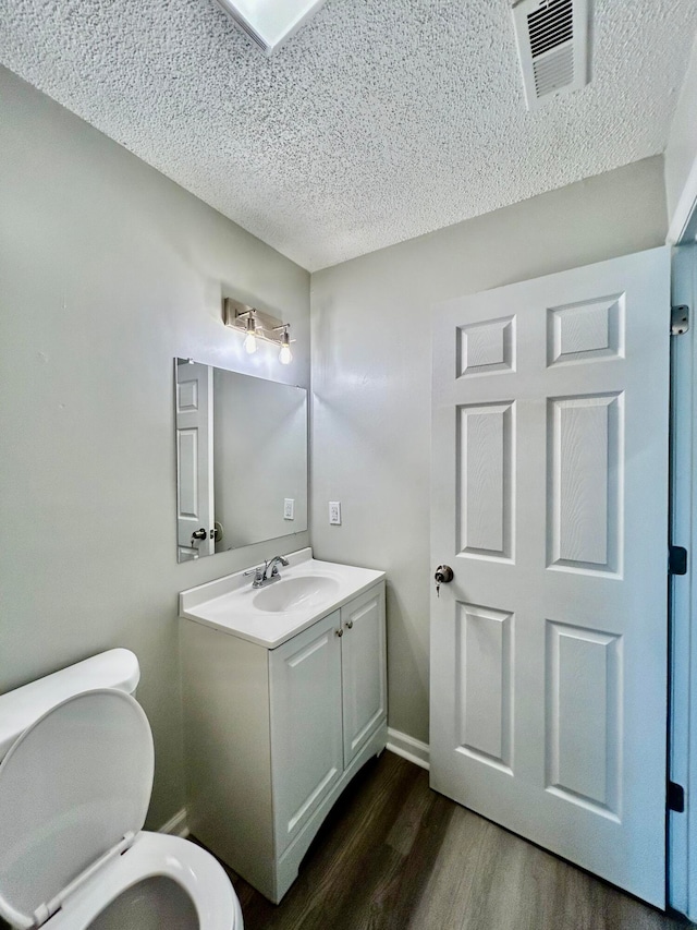 bathroom with hardwood / wood-style floors, vanity, a textured ceiling, and toilet