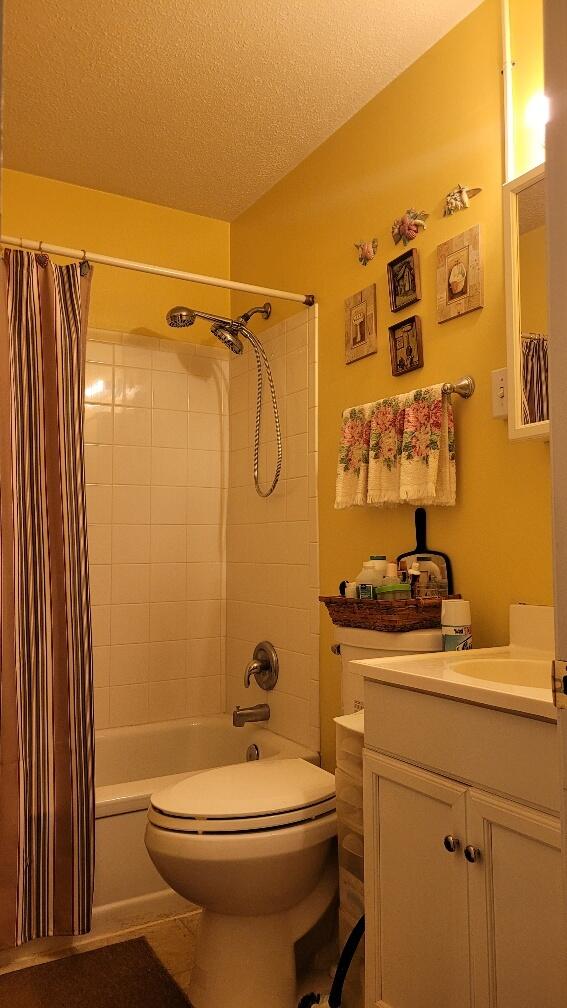 full bathroom with shower / bath combination with curtain, toilet, a textured ceiling, and vanity