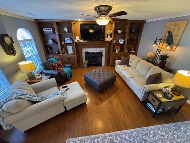 living room featuring ceiling fan, ornamental molding, a tiled fireplace, and dark wood-type flooring