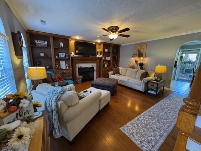 living room featuring ornamental molding, a tiled fireplace, a textured ceiling, ceiling fan, and dark hardwood / wood-style floors