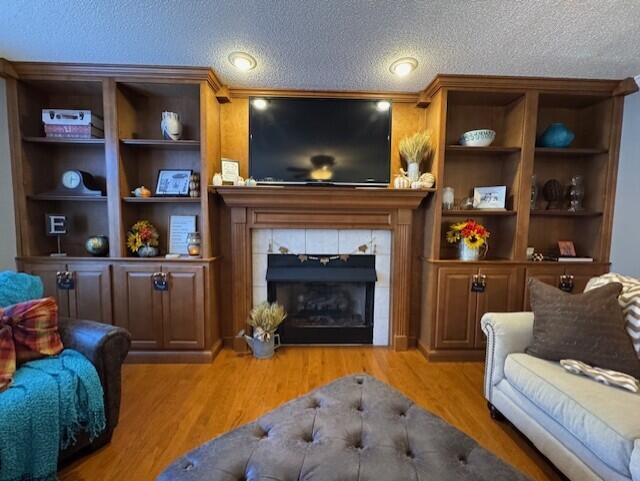 sitting room featuring a tiled fireplace, light wood-type flooring, built in features, and a textured ceiling