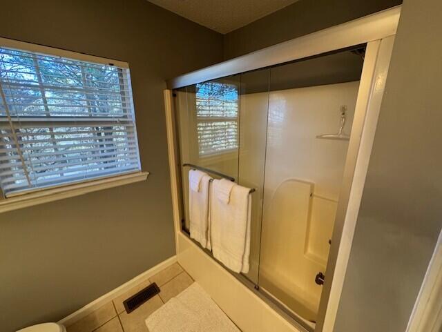 bathroom featuring tile patterned flooring, toilet, plenty of natural light, and bath / shower combo with glass door