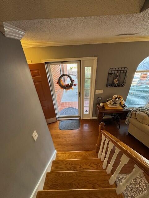 entrance foyer with a textured ceiling, wood finished floors, baseboards, stairs, and crown molding