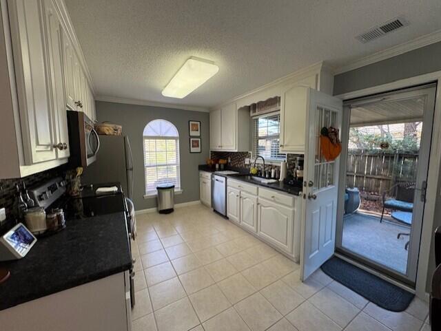 kitchen featuring white cabinets, light tile patterned floors, appliances with stainless steel finishes, tasteful backsplash, and crown molding