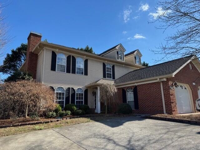 view of front of home featuring a garage, concrete driveway, brick siding, and a chimney