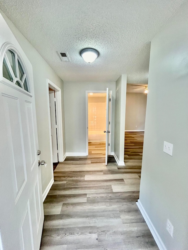 hallway with light wood-type flooring and a textured ceiling